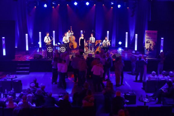 Concert avec un groupe de musique sur scène, foule dansante sous des lumières colorées.